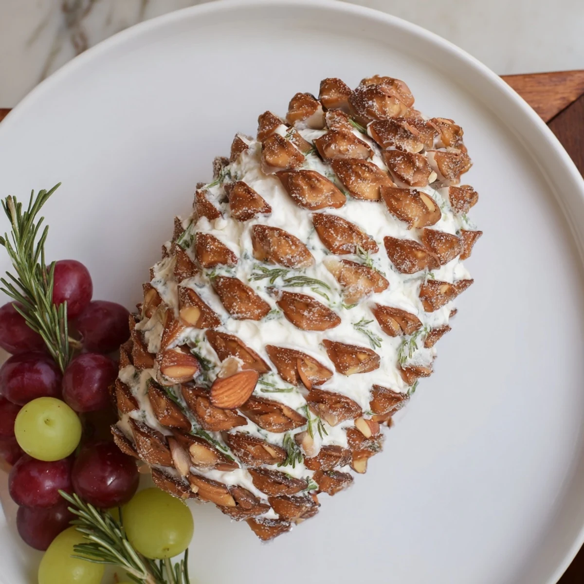 Festive Snowy Pinecone Centerpiece appetizer, a cheese-based creation, coated with almond shards for a winter look.