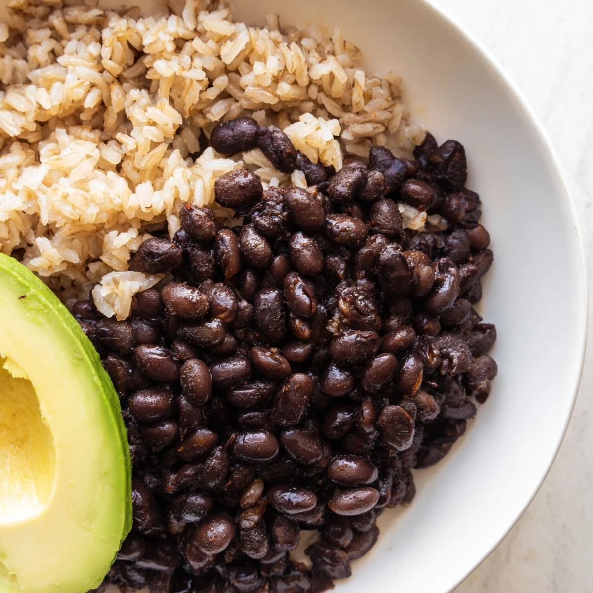 Brightly colored Brown Rice Burrito Bowl with fluffy rice, black beans, diced bell peppers, corn, cherry tomatoes, red onion, and creamy avocado slices, all topped with crumbled queso fresco and a dollop of sour cream.  