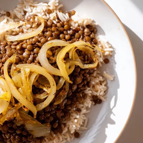 A steaming bowl of Lebanese Mjadra, lentils and rice topped with glistening caramelized onions.