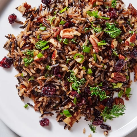 A serving of Wild Rice Harvest Salad in a white bowl shows the nutty dark rice mixed with red cranberries and golden toasted pecans.  