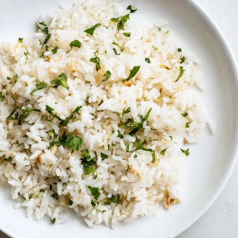 Fluffy jasmine rice, infused with fragrant garlic oil, served as a warm side dish next to colorful vegetables.