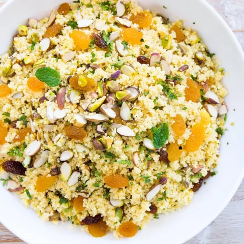 A warm bowl of Spiced Couscous Pilaf topped with toasted almonds and fresh parsley, served with a lemon wedge on a rustic table.