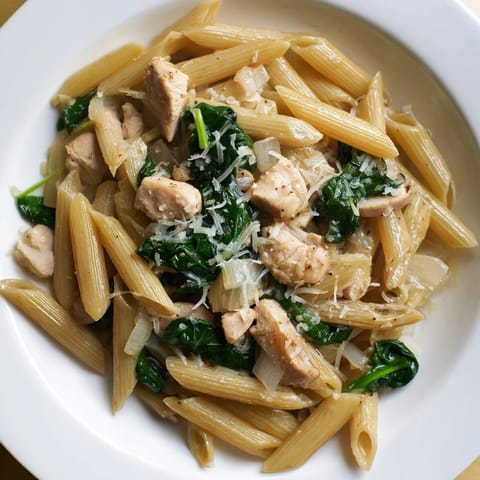 Creamy one-pot spinach and chicken pasta, ready to serve with Parmesan cheese sprinkled on top.