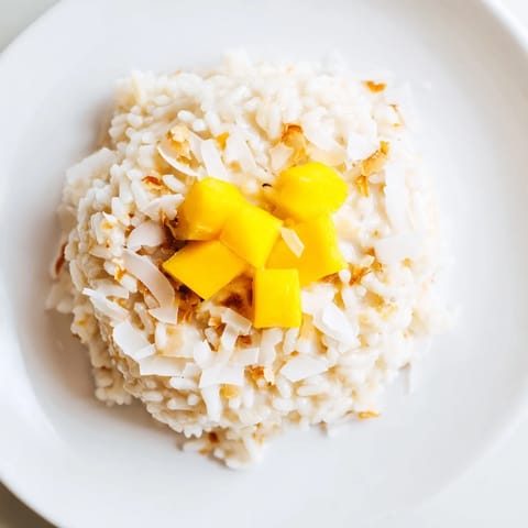 Creamy coconut rice dessert topped with toasted flakes and fresh mango, served warm in a bowl.