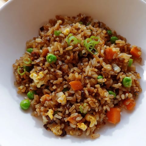 Black Garlic Fried Rice is plated in a ceramic bowl, garnished with chopped scallions and sesame seeds.  