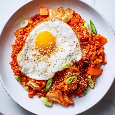 A vibrant bowl of kimchi fried rice features colorful carrots, gochujang-spiced vegetables, and a sprinkle of sesame seeds.  
