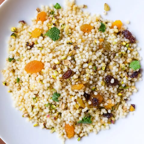 Colorful Spiced Couscous Pilaf with chopped apricots and pistachios, fluffed with a fork and ready to enjoy as a vegetarian side.