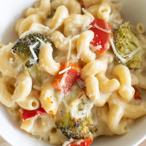 A hearty bowl of Roasted Veggie Mac & Cheese garnished with fresh parsley, showcasing tender broccoli florets and cherry tomatoes nestled in cheesy goodness.  