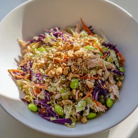Close-up of Edamame Crunch Chicken Salad topped with roasted cashews, sesame seeds, and green onions on a white plate.