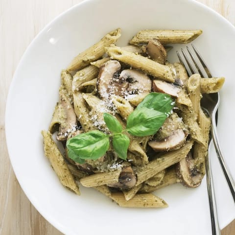A close-up of sautéed cremini mushrooms in a creamy Mushroom Pesto Pasta, served hot and ready to pair with garlic bread.