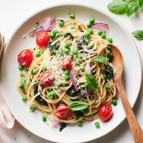 A close-up of Spring Veggie One-Pot Spaghetti topped with Parmesan and fresh basil leaves, steam rising.