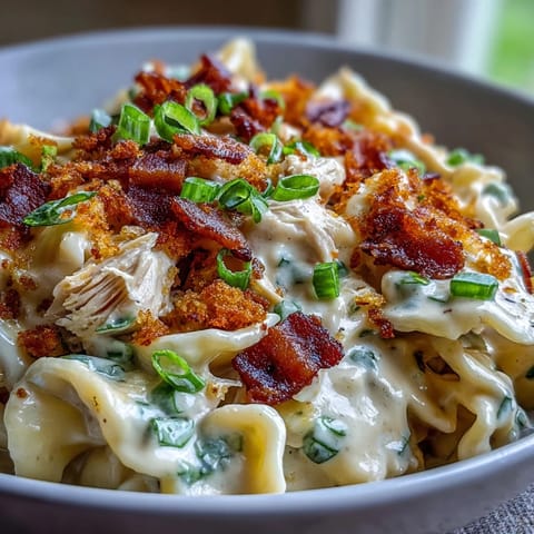 Creamy jalapeño popper chicken pasta with crispy bacon, shredded chicken, and melted cheddar cheese sauce in a skillet.