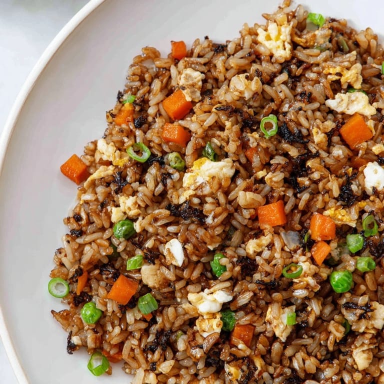 A close-up of Black Garlic Fried Rice, featuring fluffy grains with peas, carrots, and golden scrambled egg.