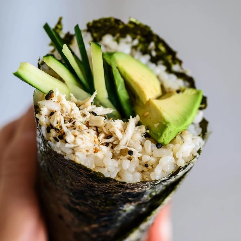 Sushi rice hand rolls with crab, avocado, and cucumber served alongside soy sauce and pickled ginger for dipping.