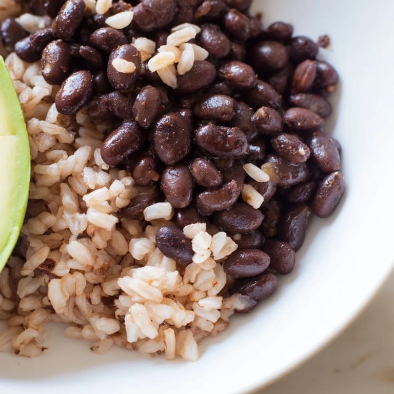 Satisfying gluten-free Brown Rice Burrito Bowl assembly with tender brown rice, hearty black beans, sautéed vegetables, sliced avocado, cheese, and sour cream, arranged neatly in a rustic bowl for a wholesome meal.