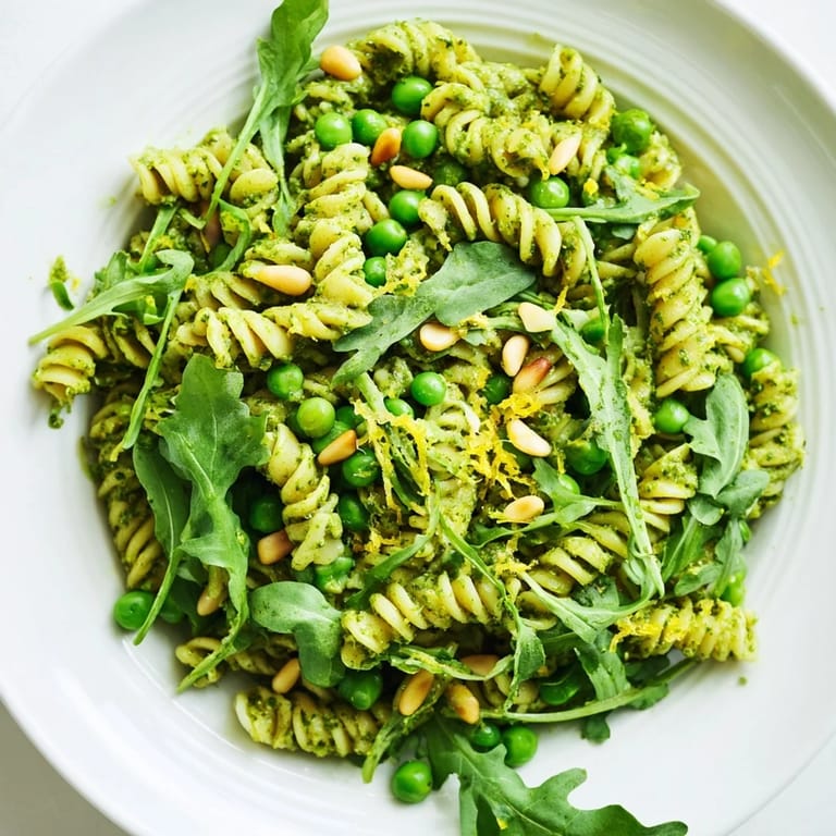 Serving suggestion of chilled Spring Green Pesto Pasta Salad topped with pine nuts and lemon zest for a fresh side dish.